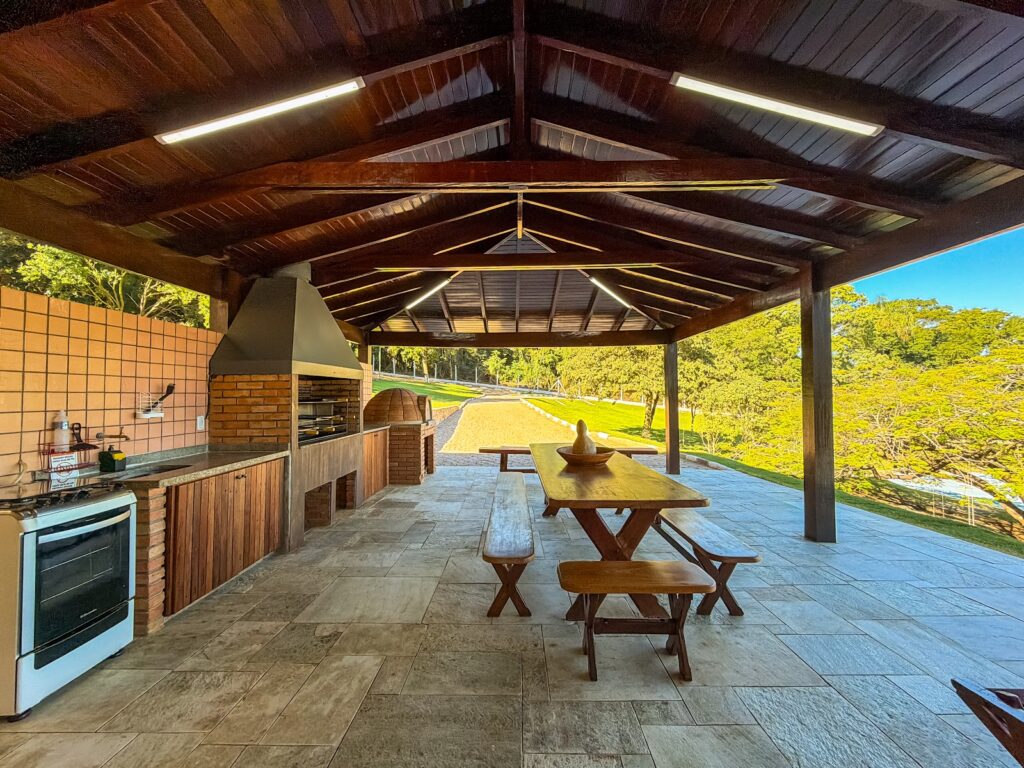 Área gourmet coberta com churrasqueira e mesa de madeira