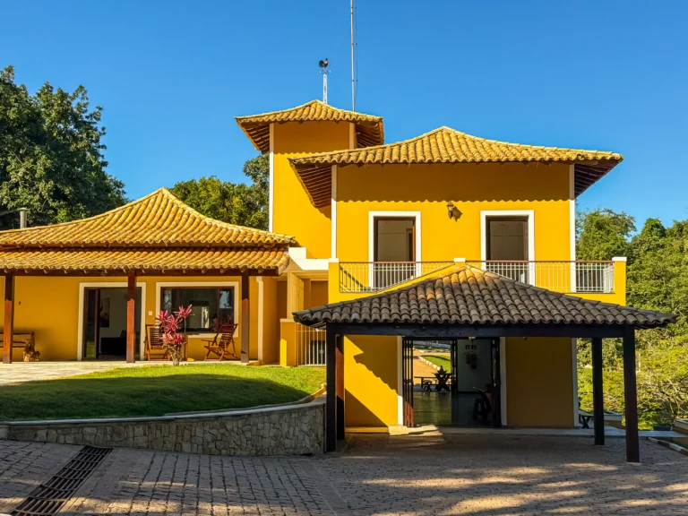 Fachada da casa principal, em amarelo, com quiosque coberto ao lado e jardim